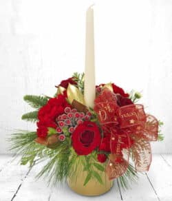 North Pole Candle Arrangement White candle surrounded by red roses, carnations, chrysanthemums, green and gold foliage, and a festive bow in a gold pot.