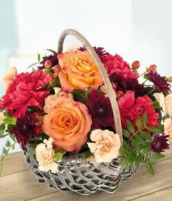 Autumnal Flower Basket Featuring Orange Roses, Cerise Carnations, Orange Spray Carnations, Burgundy Chrysanthemums, Orange Hypericum, And Pistache Foliage.