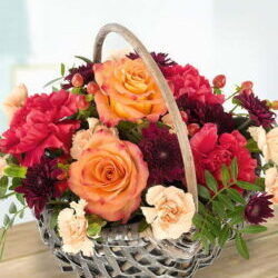 Autumnal Flower Basket Featuring Orange Roses, Cerise Carnations, Orange Spray Carnations, Burgundy Chrysanthemums, Orange Hypericum, And Pistache Foliage.