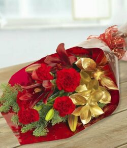 Jingle Bells Flower Bouquet Flat bouquet featuring red lilies and carnations accented by gold and green foliage, finished with a festive bow.