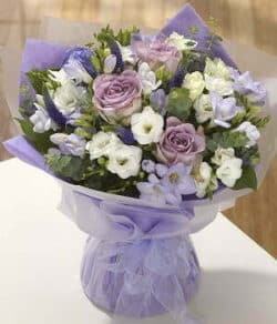 The Kenwood Flower Bouquet Hand-tied Biedermeier bouquet featuring mauve roses, seasonal lilac flowers, and white freesias arranged in a compact, elegant design.