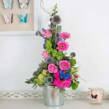 Sweet Surprise Flower Basket Featuring Pink Germini, Candy-Pink Roses, And Purple Trachelium Arranged In A Cascading, Retro-Inspired Design.