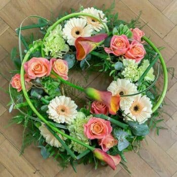 Mother Earth Wreath – Contemporary Floral Tribute Featuring Orange Roses, Peach Germini, Sleek Calla Lilies, And Structured Snake Grass Accents.