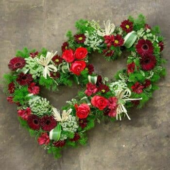 Eternal Heart Wreath Double-Heart Featuring Red Roses, Germini, Alstroemeria, Spray Carnations, Seasonal Foliage, And White Dill Accents.