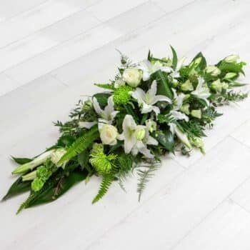 Elegant Funeral Spray Featuring White Oriental Lilies, Cream Roses, Green Shamrock Blooms, And Lush Foliage In A Luxurious Coffin Top Arrangement.