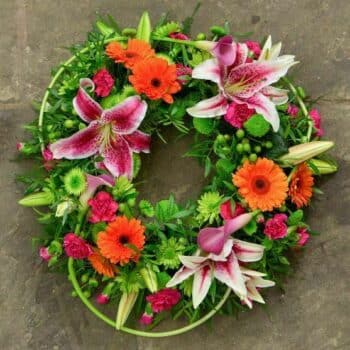 Tropical Wreath Arrangement Featuring Pink Oriental Lilies, Orange Germini, And Lime Green Spray Chrysanthemums In A Vibrant Circular Arrangement.