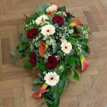 Autumnal Spray Arrangement Coffin Spray Featuring Burgundy Gerbera, Cream Calla Lilies, Eucalyptus, And Wax Flowers In A Lush, Elongated Arrangement.