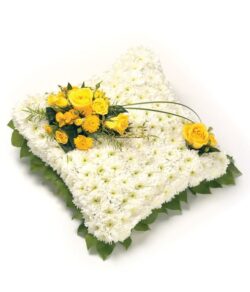 Classic White Cushion Tribute featuring a chrysanthemum base, foliage edge, and a central spray of roses, freesias, and greenery.