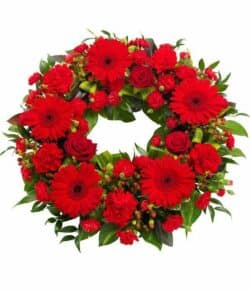 Red Wreath Tribute Circular funeral wreath featuring vibrant red roses, gerberas, and carnations with rich green foliage in an elegant design.