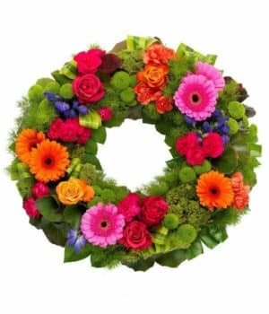 Vibrant Wreath Tribute Circular Funeral Wreath Featuring Cerise And Orange Roses, Carnations, Orange Germini, Purple Aconitum, And Green Chrysanthemums On Lush Foliage.