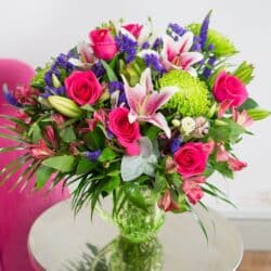 Bella Floral Bouquet featuring hot pink roses, purple veronica, and rich green foliage arranged in a vibrant, summery display