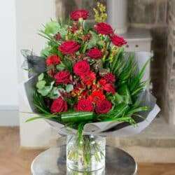 Crimson Blush Flower Bouquet with rich red roses, seasonal berries, and lush foliage arranged in a modern front-facing style