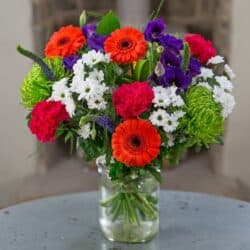 Mardi Gras Flower Bouquet featuring bright orange germini, blue Eustoma, and deep cobalt veronica arranged in a bold, colourful design.